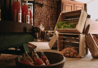Farm storage with wooden crates of vegetables, potatoes in netting, and bottles at Feather Down Fermette.