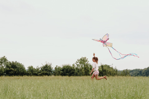 Un niño corre por un campo con césped volando una cometa colorida en Feather Down Fermette des trois tilleuls.
