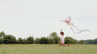 Un niño corre por un campo con césped volando una cometa colorida en Feather Down Fermette des trois tilleuls.