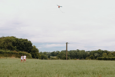 Twee kinderen laten een vlieger op in het gras bij Feather Down Fermette des trois tilleuls in Noord-Frankrijk.