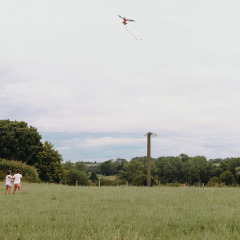Deux enfants font voler un cerf-volant dans un champ à Feather Down Fermette des trois tilleuls en Hauts-de-France.