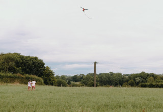 Twee kinderen laten een vlieger op in het gras bij Feather Down Fermette des trois tilleuls in Noord-Frankrijk.