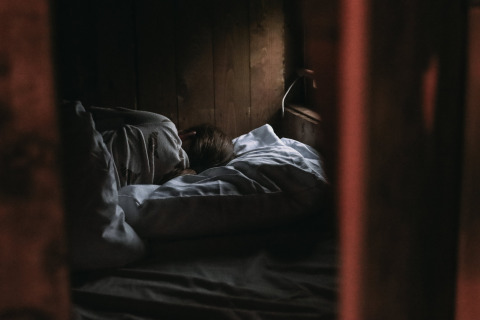 Una persona sdraiata a letto in una stanza di legno buia e accogliente alla Fermette des trois tilleuls, Francia.