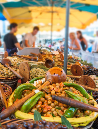 Escena de mercado cerca de Bezinghem, Hauts-de-France, Francia, con cestas de aceitunas y verduras bajo toldos coloridos.