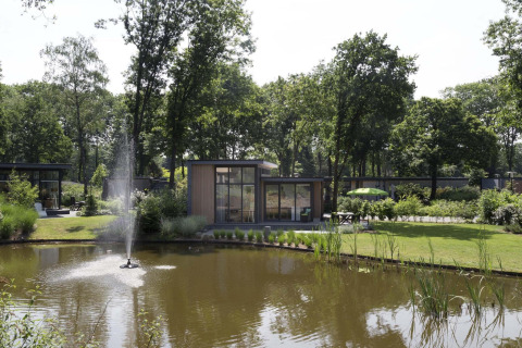 Blick auf eine moderne Lodge am Teich mit Springbrunnen im Landgoed de Scheleberg, Niederlande.