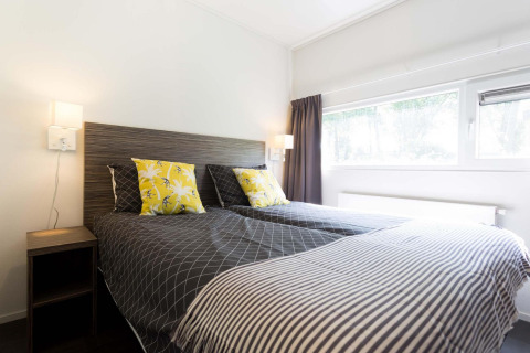 Bedroom with two single beds, bright yellow pillows, and a large window in Z Module at Landgoed de Scheleberg.