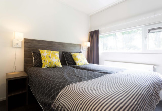 Slaapkamer met twee eenpersoonsbedden, gele kussens en groot raam in Z Module op Landgoed de Scheleberg.