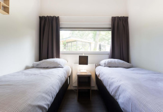 Deux lits simples aux draps gris dans la chambre Z Module au Landgoed de Scheleberg, Pays-Bas, fenêtre vitrée.