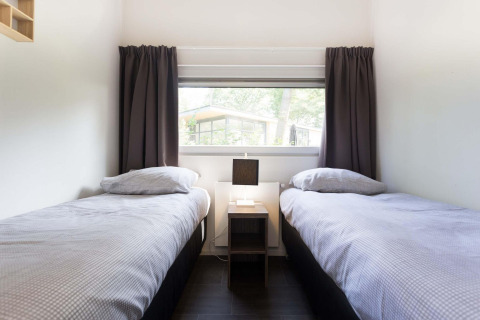 Deux lits simples aux draps gris dans la chambre Z Module au Landgoed de Scheleberg, Pays-Bas, fenêtre vitrée.