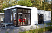 Moderne lodge Cube la Mer 4 ved Schoneveld, Holland, med store vinduer og udendørs spiseområde i skov.