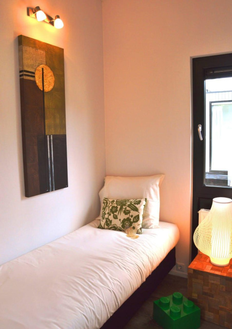 Gemütliches Zimmer mit Einzelbett, moderner Kunst, Kissen und Fenster in Cube la Mer 4, Schoneveld, Niederlande.