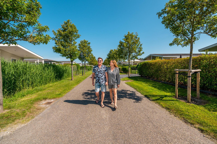 A couple walks down a tree-lined path at Cube la Mer 4 lodge in Schoneveld, the Netherlands, on a sunny day.