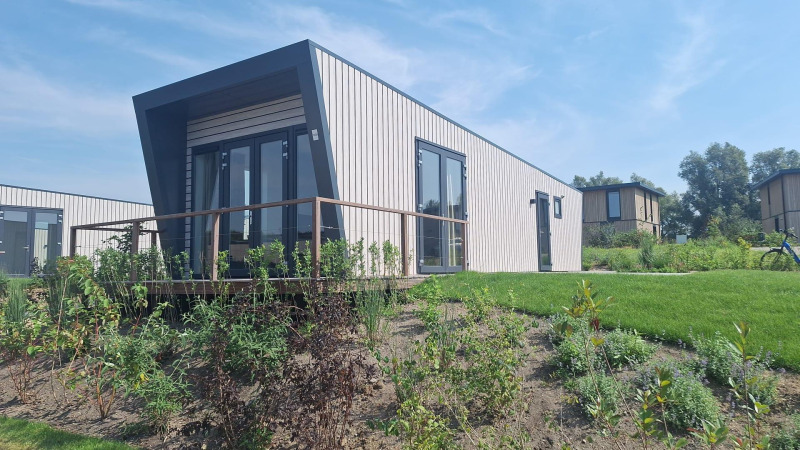 Moderna cabaña Just Nature Light en Marina Strandbad, Países Bajos, con césped verde y cielo soleado.