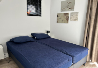Slaapkamer in Just Nature Light-lodge te Marina Strandbad Nederland, twee bedden, blauwe lakens, wanddecoratie.