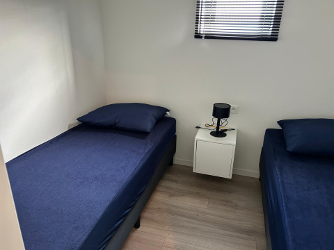 Dos camas individuales con ropa de cama azul oscuro en una habitación luminosa de Just Nature Light, Marina Strandbad, Países Bajos.
