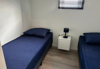 Zwei Einzelbetten mit dunkelblauer Bettwäsche in einem hellen Zimmer im Just Nature Light, Marina Strandbad, Niederlande.