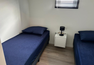 Dos camas individuales con ropa de cama azul oscuro en una habitación luminosa de Just Nature Light, Marina Strandbad, Países Bajos.