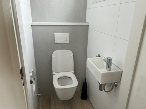 Toilettes modernes avec WC suspendu, petit lavabo et sol en bois chez Just Nature Light aux Pays-Bas.