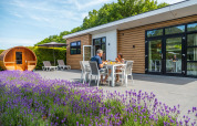 Par nyder måltid udenfor Deluxe Sauna-hytte ved EuroParcs Noordwijkse Duinen, omgivet af lavendel.