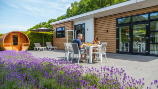 Couple dînant devant une cabane Deluxe Sauna à EuroParcs Noordwijkse Duinen, lavande au premier plan.