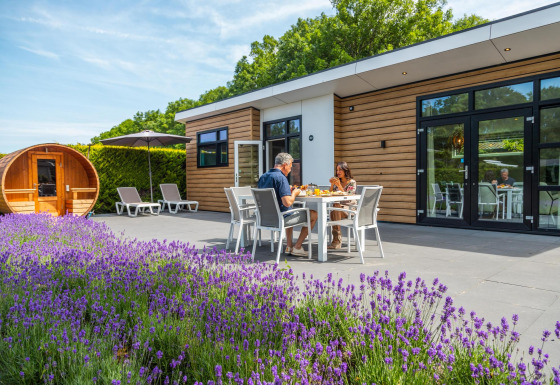 Paar genießt Essen auf der Terrasse der Deluxe Sauna in EuroParcs Noordwijkse Duinen mit Lavendelblick.