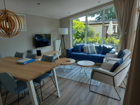 Moderne woonkamer in Deluxe Sauna-hut bij EuroParcs Noordwijkse Duinen met groot raam en blauwe zetel.