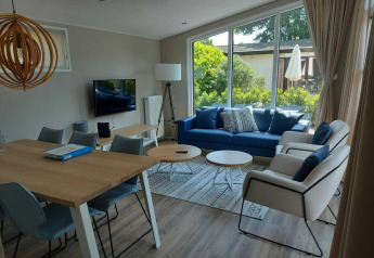 Moderne woonkamer in Deluxe Sauna-hut bij EuroParcs Noordwijkse Duinen met groot raam en blauwe zetel.