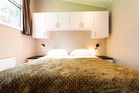 Dormitorio de la cabaña Deluxe Sauna con ropa de cama blanca y armarios superiores en EuroParcs Noordwijkse Duinen.