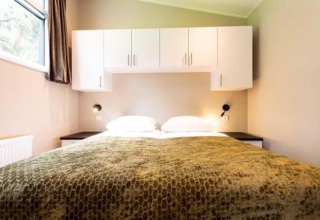 Dormitorio de la cabaña Deluxe Sauna con ropa de cama blanca y armarios superiores en EuroParcs Noordwijkse Duinen.