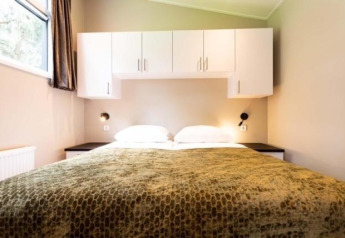 Slaapkamer in Deluxe Sauna-huisje met wit beddengoed en hangkasten bij EuroParcs Noordwijkse Duinen.