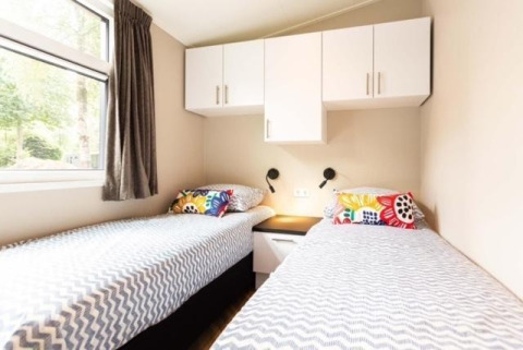 Chambre avec deux lits simples, armoires blanches et coussins colorés à Deluxe Sauna à EuroParcs Noordwijkse Duinen.