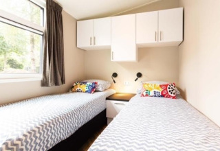 Chambre avec deux lits simples, armoires blanches et coussins colorés à Deluxe Sauna à EuroParcs Noordwijkse Duinen.