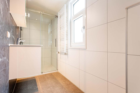 Bagno moderno con doccia in vetro, ampia finestra e piastrelle bianche alla Deluxe Sauna di EuroParcs Noordwijkse Duinen.