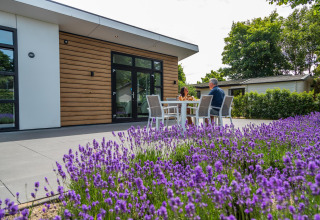 Pareja sentada en una mesa exterior frente a la cabaña Deluxe Sauna en EuroParcs Noordwijkse Duinen, Países Bajos.