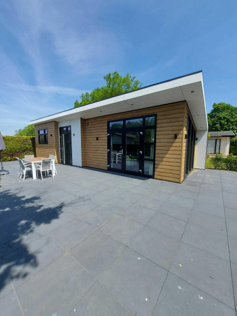 Moderne Deluxe Sauna blokhut met houten gevel en ruim terras bij EuroParcs Noordwijkse Duinen, Nederland.
