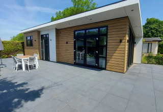 Moderne hytte med træbeklædning og store vinduer på en stor terrasse ved EuroParcs Noordwijkse Duinen.