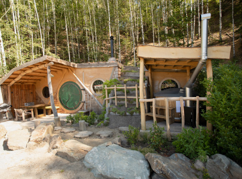 Hobbit House 1, una pequeña casa inspirada en El Señor de los Anillos, con puerta verde y ventanas redondas.