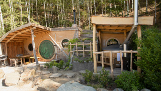 Hobbit House 1, una pequeña casa inspirada en El Señor de los Anillos, con puerta verde y ventanas redondas.
