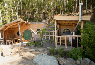 Hobbit House 1, een tiny house in hobbitstijl met groene ronde deur, midden in een bosrijke omgeving.