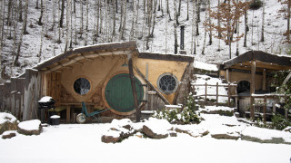Hobbit House 1 met sneeuw in het bos van Limburg, België, met een ronde groene deur en knusse sfeer.