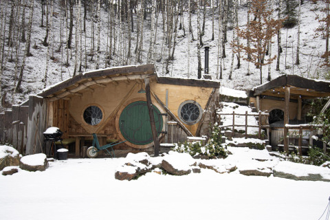 Hobbit House 1 met sneeuw in het bos van Limburg, België, met een ronde groene deur en knusse sfeer.