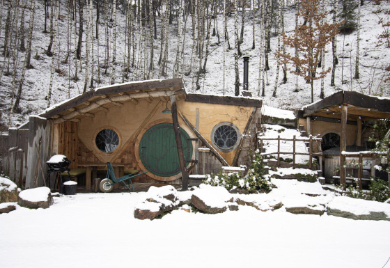 Hobbit House 1 met sneeuw in het bos van Limburg, België, met een ronde groene deur en knusse sfeer.