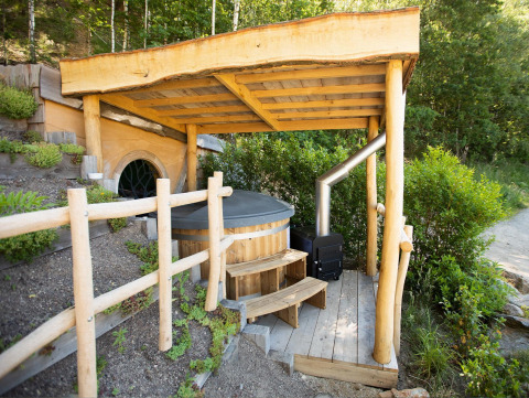 Casa Hobbit 1 en Cosy Cabins, bosque de Limburg, Bélgica, con terraza techada y bañera de madera al aire libre.