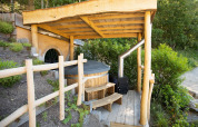 Casa Hobbit 1 en Cosy Cabins, bosque de Limburg, Bélgica, con terraza techada y bañera de madera al aire libre.