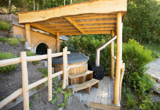 Casa Hobbit 1 en Cosy Cabins, bosque de Limburg, Bélgica, con terraza techada y bañera de madera al aire libre.