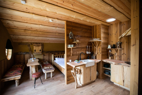 Interior de madera de Hobbit House 1 en Cosy Cabins, bosque de Limburgo, Bélgica, con cocina y cama.