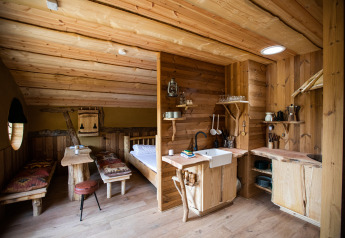 Innenraum aus Holz im Hobbit House 1 bei Cosy Cabins im Wald von Limburg, Belgien, mit Küche und Bett.