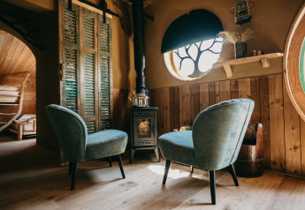 Two cozy chairs by a wood stove in Hobbit House 1 at Cosy Cabins, Limburg, Belgium forest retreat.