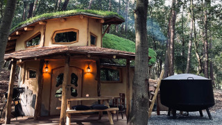 Sfeervolle Hobbit House lodge in het bos met grasdak, houten veranda en rustieke uitstraling.