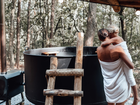 Madre e hijo envueltos en toallas junto a una bañera al aire libre en Hobbit House, Cosy Cabins, Limburg, Bélgica.